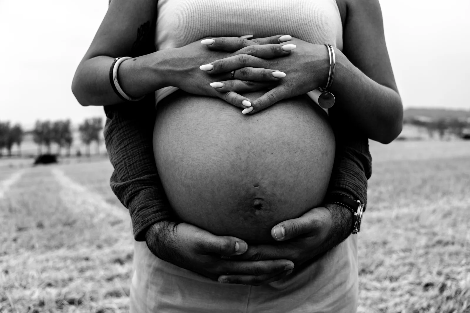 Des mains entourent un ventre rond dans un portrait en noir et blanc.