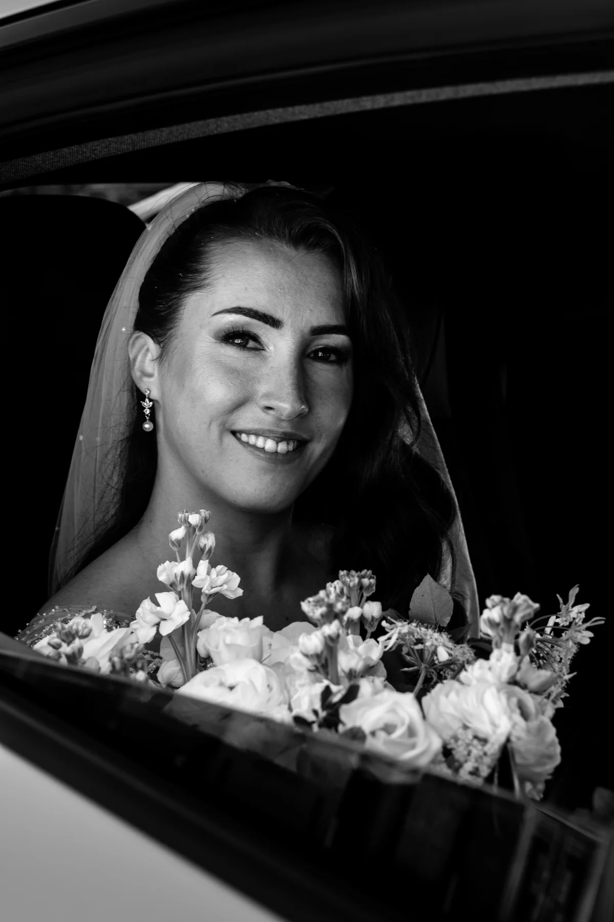 Portrait en noir et blanc d’une mariée souriante, son bouquet au premier plan.
