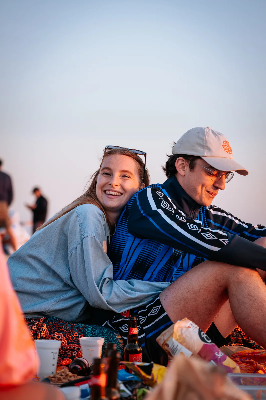 Un couple partage un moment complice assis dans le sable à la lumière du soir.
