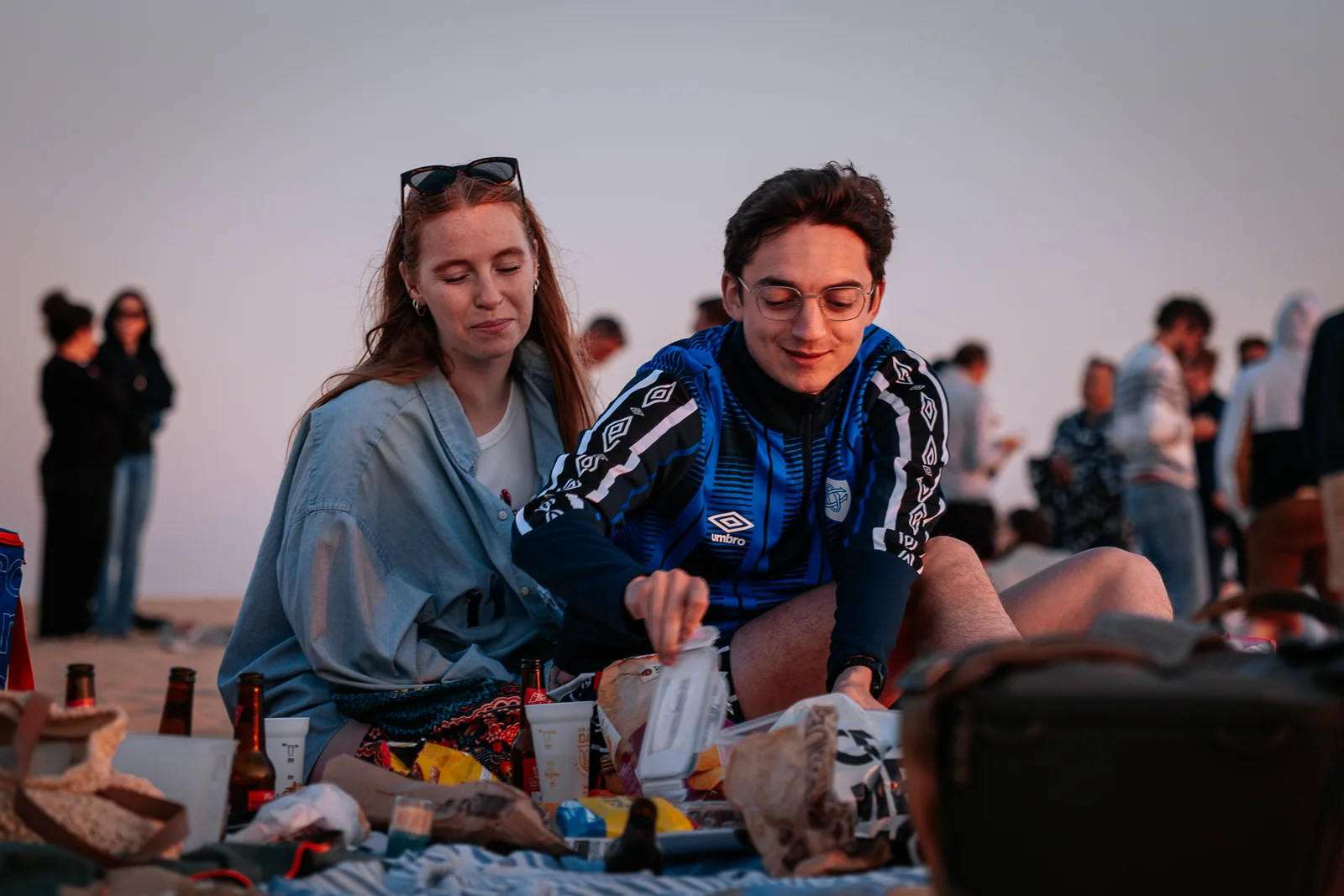 Deux proches partagent un pique-nique sur la plage à la lumière du soir.