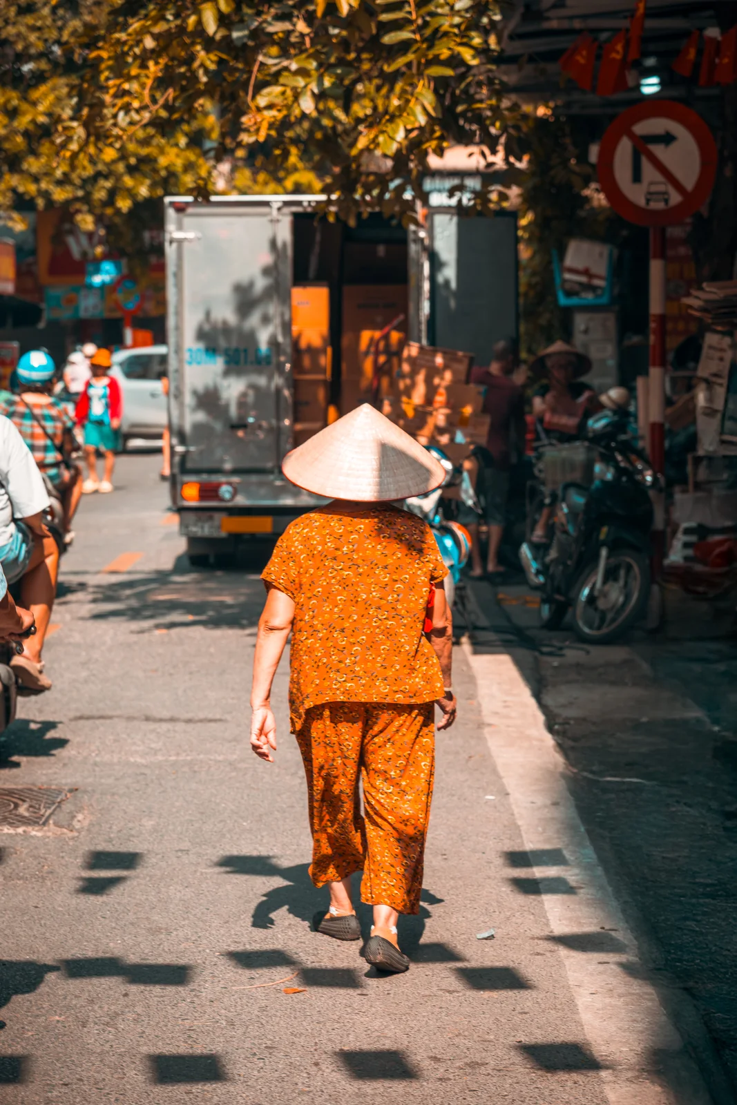 Une femme en tenue orange marche dans une rue animée du Vietnam.
