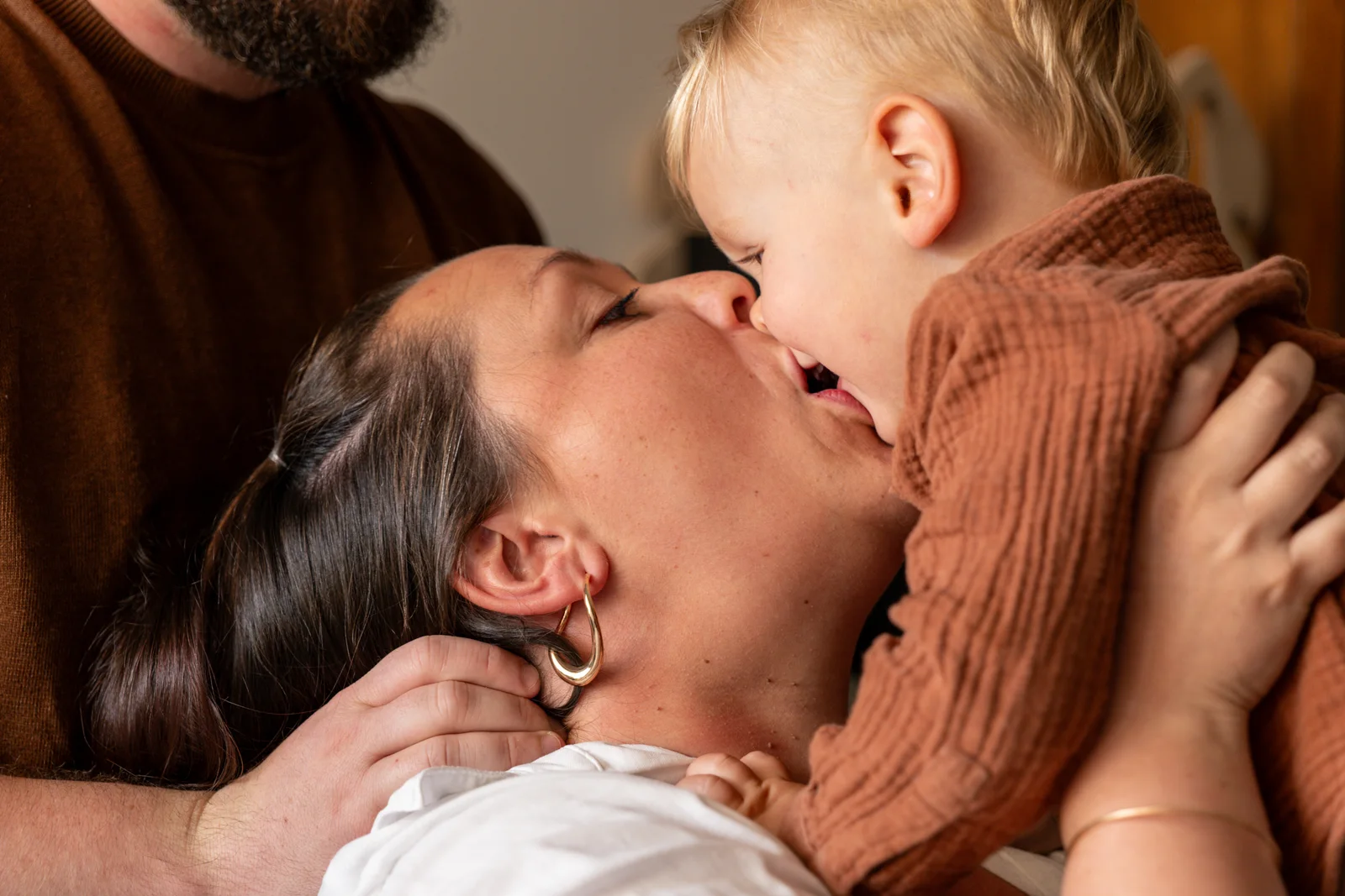 Une mère embrasse son jeune enfant dans les bras, sous le regard du père.