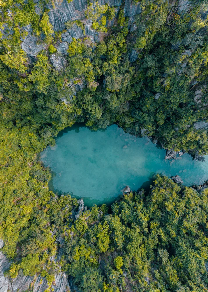 Un lagon turquoise entouré de falaises et de végétation, vu du ciel.