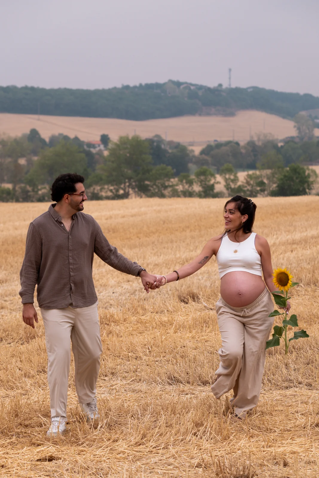 Un couple avance main dans la main au milieu d’un champ de blé.