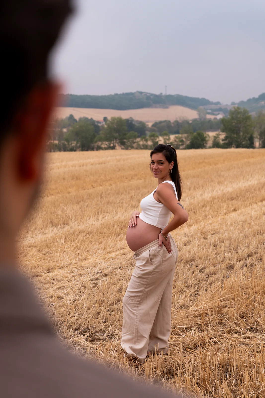 Une future mère pose sereinement dans les blés, une main sur son ventre.
