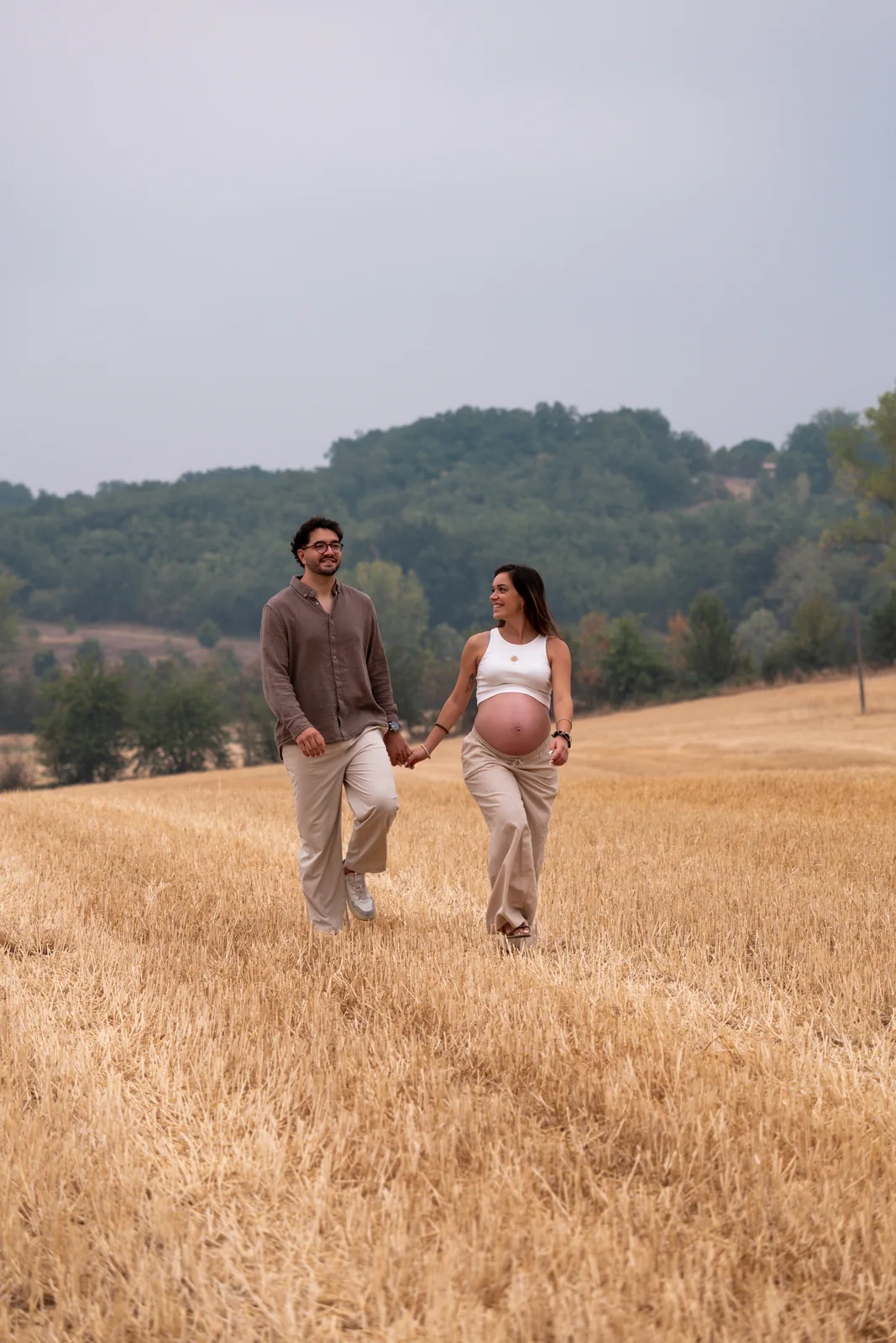Les futurs parents marchent ensemble dans un paysage de campagne.