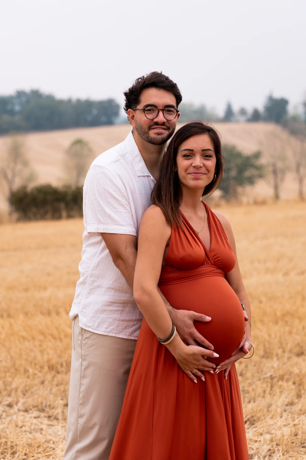 Une future mère vêtue de rouge se laisse enlacer dans les blés.