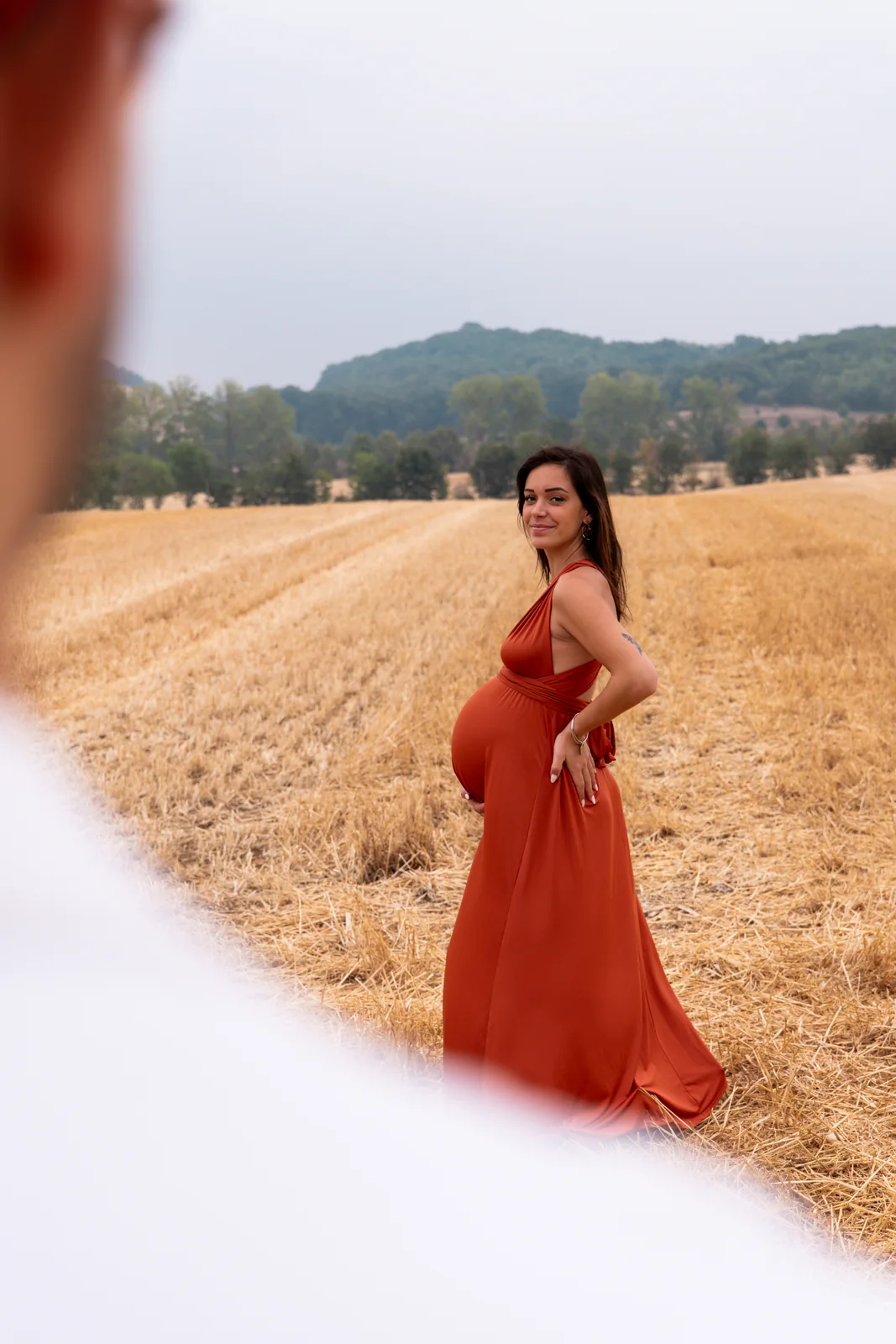 Une future mère en robe rouge marche seule le long d’un chemin dans les blés.