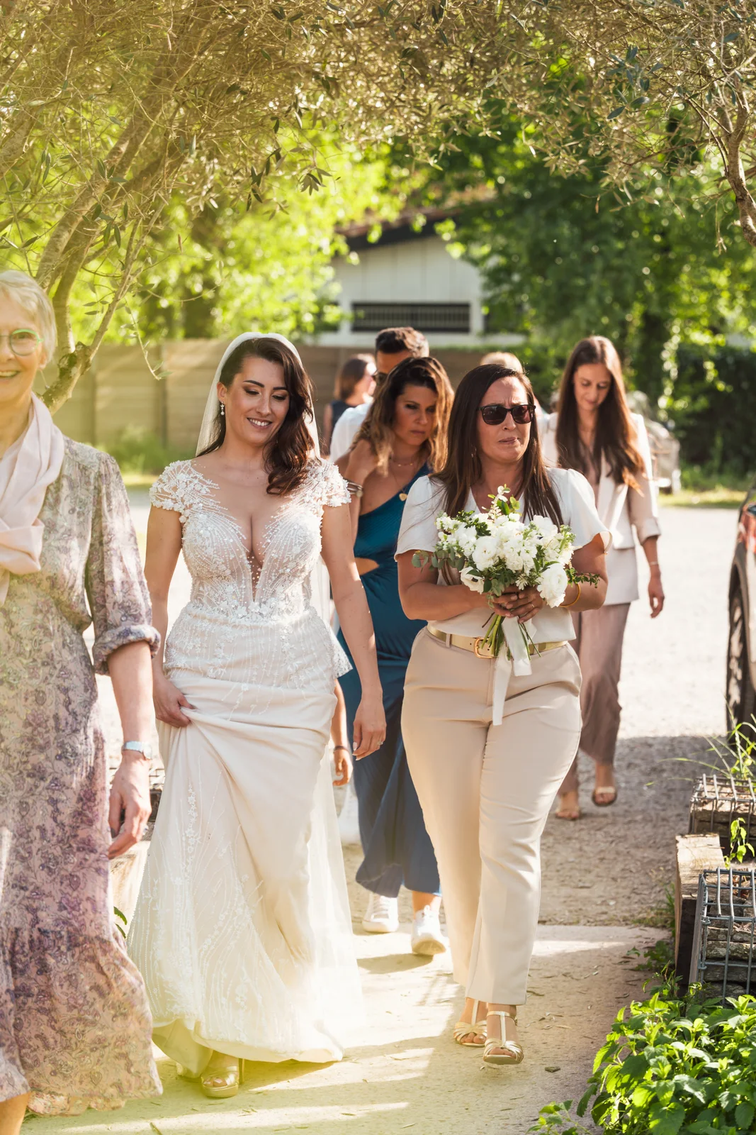 Une mariée avance au soleil, entourée de ses proches.