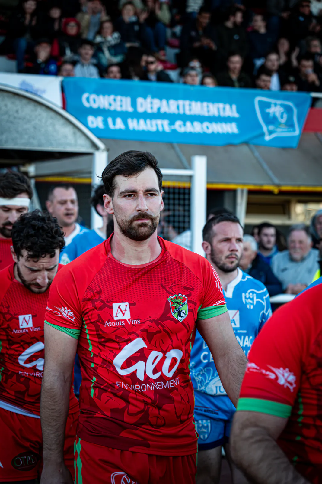 Un joueur de rugby au regard concentré avance avec son équipe devant les tribunes.