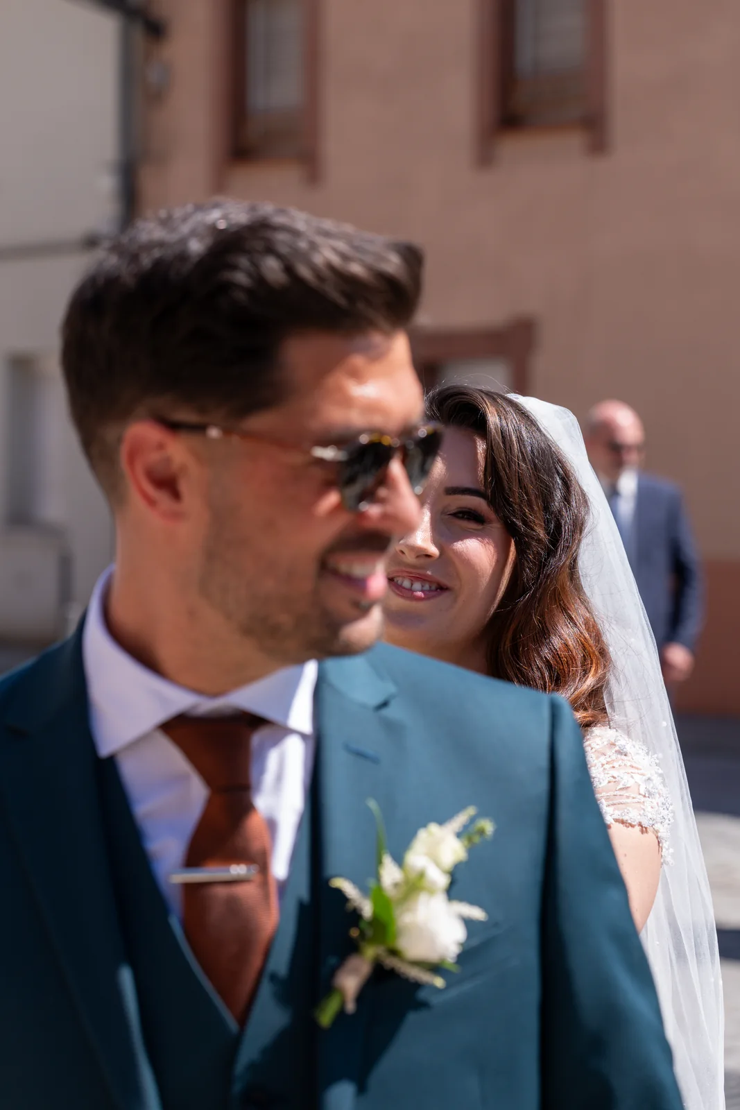 Le marié avance au soleil tandis que la mariée sourit juste derrière lui.