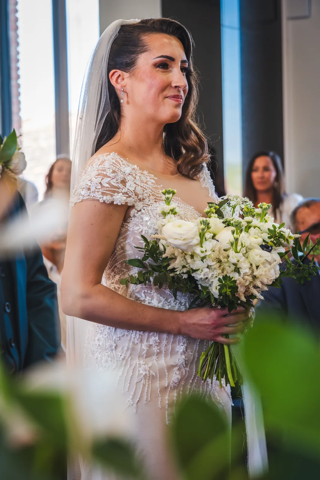 Le bouquet blanc et le corsage brodé de la mariée saisis dans la lumière de la cérémonie.