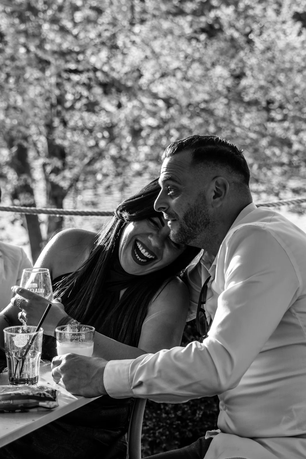 Deux proches rient ensemble à table pendant la réception, en noir et blanc.