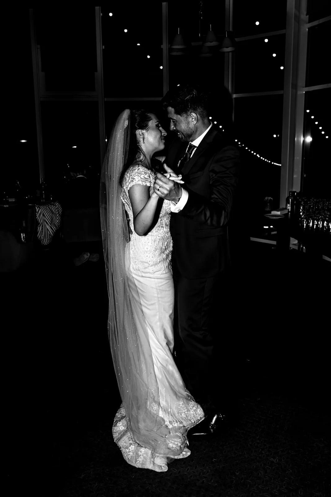 Les mariés se retrouvent dans une étreinte sous les lumières de la nuit, en noir et blanc.
