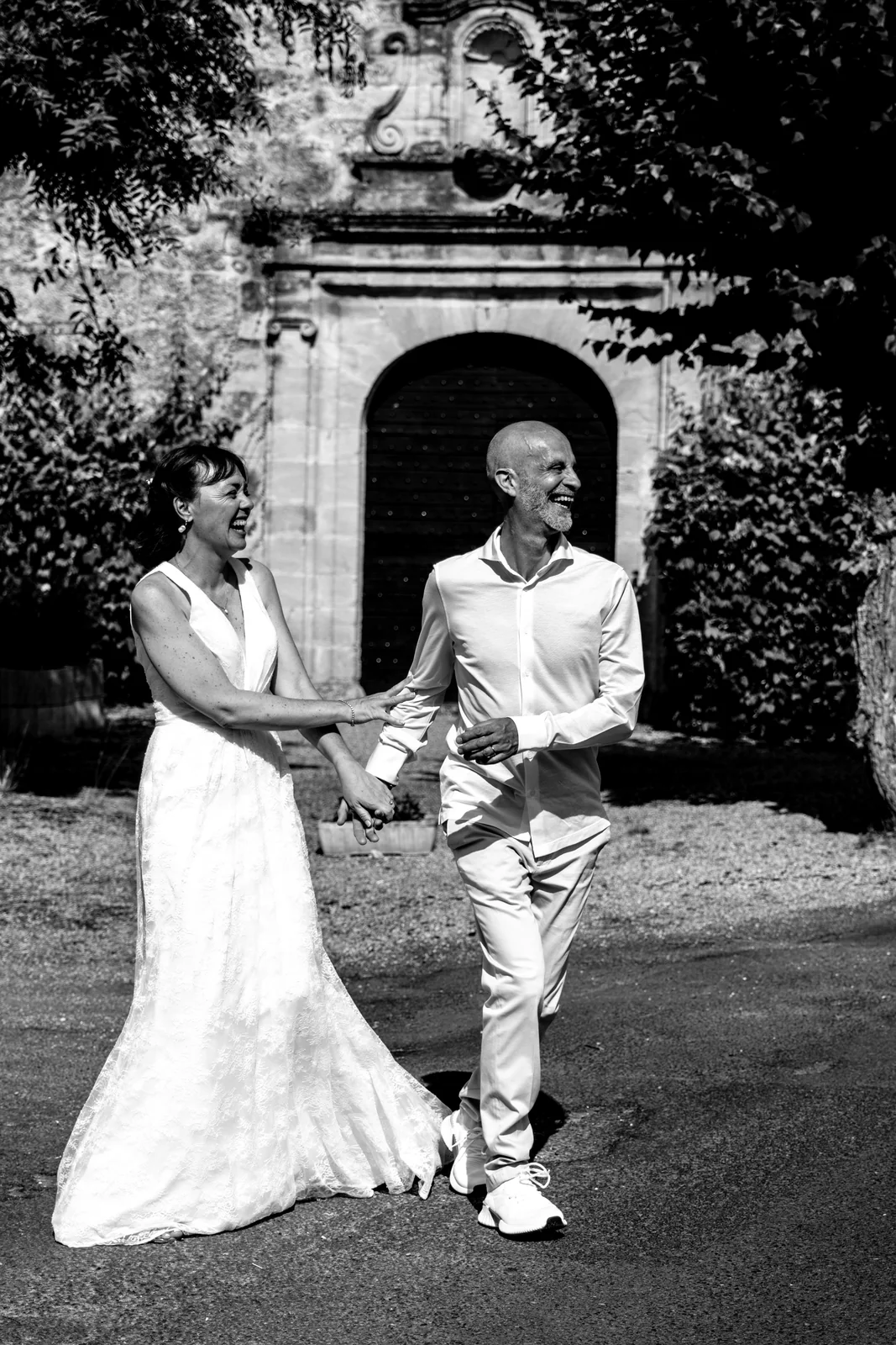 Deux mariées se tiennent par la main dans un jardin, en noir et blanc.