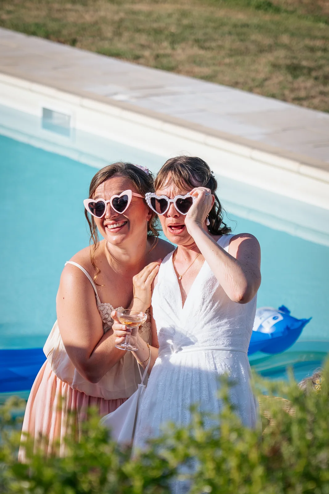 Deux invitées s’amusent avec des lunettes en forme de cœur près de la piscine.