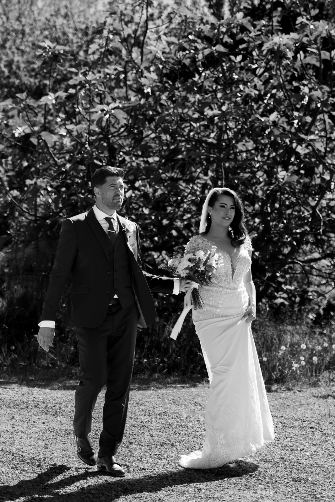 Un couple de jeunes mariés marche côte à côte au soleil dans un portrait en noir et blanc.